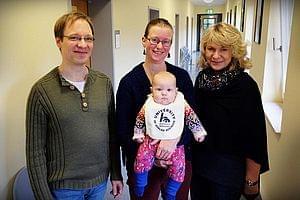 Hochschul-Lätzchen-Übergabe Eltern mit Baby und die Gleichstellungsbeauftragte der HSN stehen nebeneinander. Das Baby trägt das HSN-Lätzcen.