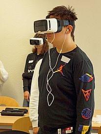 Eine Person trägt eine VR-Brille. Eine weitere Person mit VR-Brille steht dahinter.